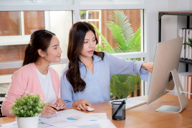 İki Asyalı iş kadını veri analizi pazarlama finansmanı ile ilgili işbirliği yapıyor, grafiklerle birlikte bilgisayar, takım çalışması ve pazarlama stratejisi planlaması üzerinde çalışıyorlar..