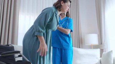 Tekerlekli sandalyeden kanepeye taşınırken hareket kabiliyeti kısıtlı olan bakıcı, evdeki oturma odasında tekerlekli sandalyeden kanepeye taşınan hastaya yardım eden hemşire, rehabilitasyon ve yardım..