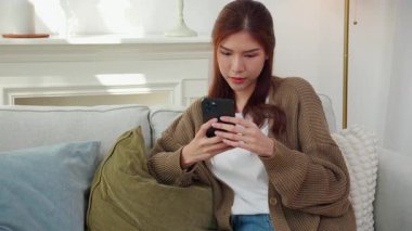 Modern evdeki oturma odasında telefonla konuşurken gülümseyen Asyalı genç kadın, yaşam tarzını rahatlat, konuşmaktan zevk alan mutlu kadın, neşeli yüz ifadesi, eğlenceli telefon konuşması yapan mutlu kadın..