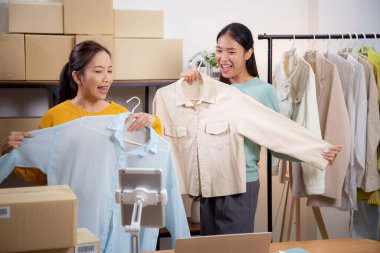 İki genç Asyalı kadın online giyim mağazasında yaşarken, evde sosyal tabletle giysi satışı yaparken, girişimci çevrimiçi kıyafet satışı ve sunumu için çevrimiçi satış yapıyor..