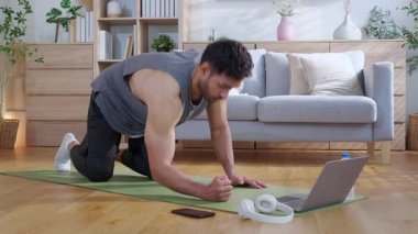 Genç Asyalı adam evde oturma odasında kalas egzersizi yaparken dizüstü bilgisayarda dayanıklılık ve motivasyonla antrenman eğitimi alırken yoga minderinde adam eğitim tahtası, dijital fitness yaşam tarzı..