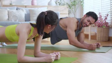 Genç Asyalı çift evdeki oturma odasında beşlik çakarken tahtayla antrenman yapıyor. Erkek ve kadın birlikte meydan okuma, motivasyon ve sağlık için kas gücü eğitimi alıyor..