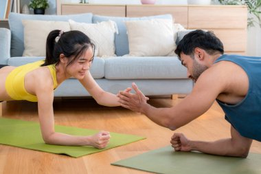 Genç Asyalı çift evdeki oturma odasında beşlik çakarken tahtayla antrenman yapıyor. Erkek ve kadın birlikte meydan okuma, motivasyon ve sağlık için kas gücü eğitimi alıyor..