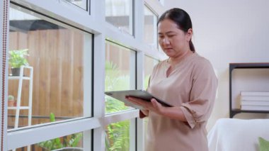 Evde Al ile sohbet etmek için tablet kullanan üst düzey Asyalı kadın, dijital yaşam tarzı, iletişim ve teknoloji, çevrimiçi bağlantı, akıllı aletten hoşlanan kadın, sanal asistan..
