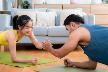 Genç Asyalı çift evdeki oturma odasında beşlik çakarken tahtayla antrenman yapıyor. Erkek ve kadın birlikte meydan okuma, motivasyon ve sağlık için kas gücü eğitimi alıyor..