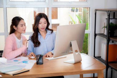 İki Asyalı iş kadını veri analizi pazarlama finansmanı ile ilgili işbirliği yapıyor, grafiklerle birlikte bilgisayar, takım çalışması ve pazarlama stratejisi planlaması üzerinde çalışıyorlar..