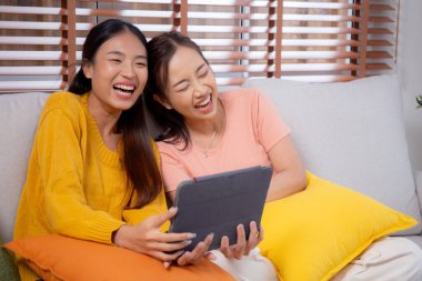 Oturma odasında dijital tablet kullanan iki genç Asyalı kadın, sosyal medyayı internet tableti ve konuşma mesafesi için kullanan kadın, yaşam tarzı kavramı.