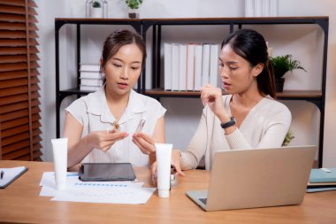 Ofiste kozmetik ürünü ya da kremi test eden ve araştıran iki Asyalı iş kadını. Cilt tasarımı, geliştirme ve iş dünyasından iki iş kadını..