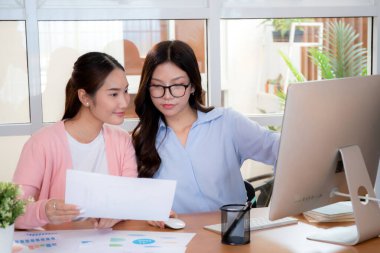 İki Asyalı iş kadını veri analizi pazarlama finansmanı ile ilgili işbirliği yapıyor, grafiklerle birlikte bilgisayar, takım çalışması ve pazarlama stratejisi planlaması üzerinde çalışıyorlar..