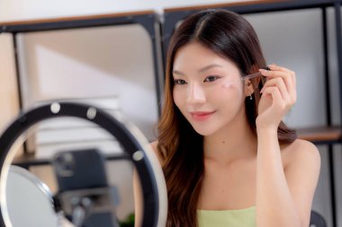 Güzellik değerlendirmesi için sosyal medyada serum, cilt bakımı ve kozmetik içeriği sergileyen Asyalı genç bir kadın güzellik ürünleri ve canlı yayın, yaşam tarzı ve cilt bakımı.