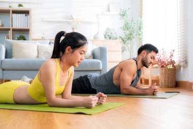 Genç Asyalı çift evdeki oturma odasında beşlik çakarken tahtayla antrenman yapıyor. Erkek ve kadın birlikte meydan okuma, motivasyon ve sağlık için kas gücü eğitimi alıyor..