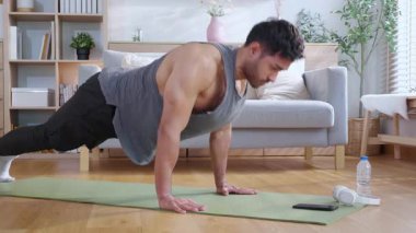 Genç Asyalı adam evde oturma odasında kararlılıkla şınav çekiyor yoga minderi eğitimi alıyor vücut geliştirme gücü ve sağlıklı yaşam tarzı için uygunluk, egzersiz rutini, kişisel bakım..