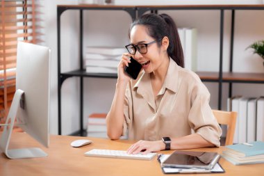 Genç Asyalı iş kadını ofis telefonuyla konuşurken masaüstü bilgisayarı kullanıyor, iş kadını telefon, iş ya da danışmanlık yaparken masaüstü bilgisayarıyla çalışıyor.
