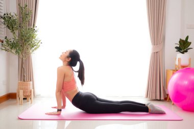 Evde yoga minderinde kaslarını esneterek yoga yapan Asyalı genç bir kadın, meydan okuma ve motivasyonla pilates yapan bir kadın, sağlık, spor ve refah için egzersiz yapan bir kadın..