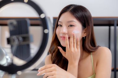 Genç Asyalı kadın kozmetik ürünlerini sosyal medya platformunda takipçiler, krem ya da losyonu canlı yayında inceleyen, etkileyen ve gözden geçiren kadınlar için heyecan verici bir şekilde sunup gözden geçiriyor..