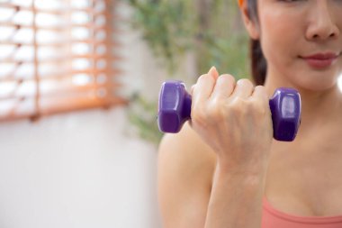 Spor giyinen genç bir kadın. Oturma odasındaki güç için halterlerle spor yapıyor. Azimli bir kadın antrenmanı ve kaldırmayla mücadele ediyor..