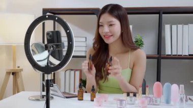 Genç Asyalı bir kadın sosyal medyaya damlalık serumu uyguluyor, içerik yaratıcısı, özbakım ve kozmetik ürünleri gözden geçirme, cilt bakımı ve kozmetik ürünleri, etki yaratan ürünleri gözden geçiriyor..