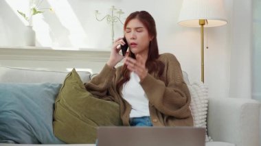 Modern evdeki oturma odasında telefonla konuşurken gülümseyen Asyalı genç kadın, yaşam tarzını rahatlat, konuşmaktan zevk alan mutlu kadın, neşeli yüz ifadesi, eğlenceli telefon konuşması yapan mutlu kadın..