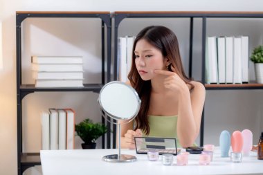 Genç Asyalı kadın aynayla cilt sorununu kontrol etmek için aynaya bakıyor evde endişe ifadesi, cilt bakımı ve güzellik endişesi, cilt bakımı ve sağlık, stres ile yüz derisini inceleyen kadın..
