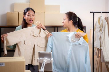 İki genç Asyalı kadın online giyim mağazasında yaşarken, evde sosyal tabletle giysi satışı yaparken, girişimci çevrimiçi kıyafet satışı ve sunumu için çevrimiçi satış yapıyor..