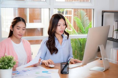 İki Asyalı iş kadını veri analizi pazarlama finansmanı ile ilgili işbirliği yapıyor, grafiklerle birlikte bilgisayar, takım çalışması ve pazarlama stratejisi planlaması üzerinde çalışıyorlar..