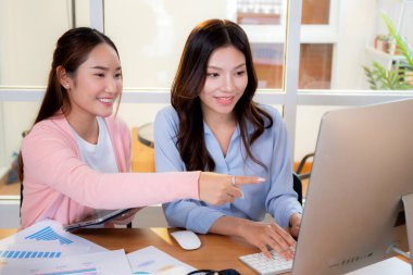 İki Asyalı iş kadını veri analizi pazarlama finansmanı ile ilgili olarak merkez ofisteki grafikler, bilgisayar ekranı, takım çalışması ve pazarlama stratejisi planlamasında birlikte çalışıyorlar..