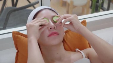 Genç Asyalı kadın evinde cilt bakımı sırasında salatalık dilimi ile kanepeye uzanıyor. Güzellik ve güzellik. Huzurlu ve rahat..