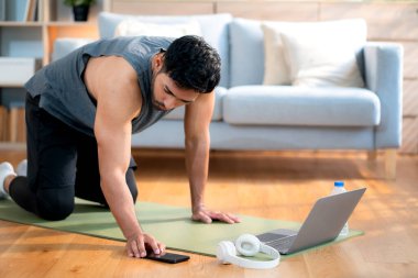 Genç Asyalı adam evde oturma odasında kalas egzersizi yaparken dizüstü bilgisayarda dayanıklılık ve motivasyonla antrenman eğitimi alırken yoga minderinde adam eğitim tahtası, dijital fitness yaşam tarzı..