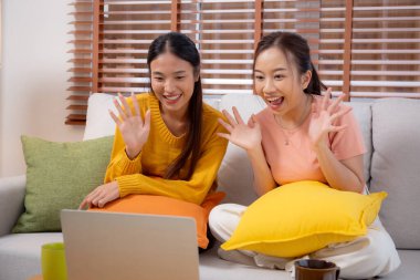 Kanepede oturan iki genç Asyalı kadın evdeki oturma odasında dizüstü bilgisayar kullanıyor, sosyal medyayı internet ve sohbet için kullanıyor, yaşam tarzı kavramı..
