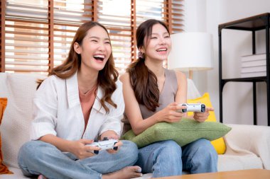 İki Asyalı kadın, evdeki rahat bir oturma odasında bilgisayar oyunu oynuyorlar. Eğlence, arkadaşlık ve neşeli bir yaşam tarzı. Asyalı arkadaşlar, eğlence ve oyun paylaşımının keyfini çıkarıyorlar..