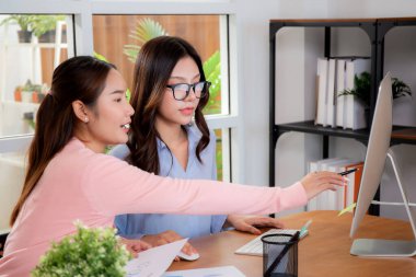 İki Asyalı iş kadını veri analizi pazarlama finansmanı ile ilgili işbirliği yapıyor, grafiklerle birlikte bilgisayar, takım çalışması ve pazarlama stratejisi planlaması üzerinde çalışıyorlar..