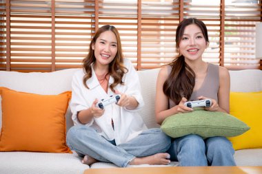 İki Asyalı kadın, evdeki rahat bir oturma odasında bilgisayar oyunu oynuyorlar. Eğlence, arkadaşlık ve neşeli bir yaşam tarzı. Asyalı arkadaşlar, eğlence ve oyun paylaşımının keyfini çıkarıyorlar..