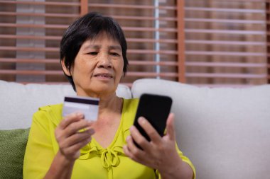 Kıdemli Asyalı kadın internet üzerinden akıllı telefon alışverişi yapıyor. İnternete kredi kartı alıyor. Akıllı telefon, alım-satım, ödeme, iş ve finans ile kadın ödemesi yapıyor..