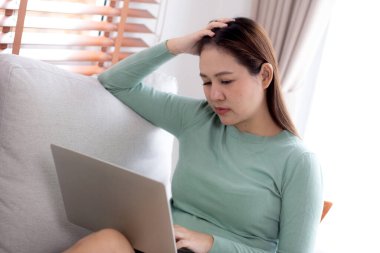 Genç Asyalı iş kadını evde stresli ve hayal kırıklığına uğramış bir şekilde dizüstü bilgisayarla çalışıyor, iş kadını defterinde üzgün ve yorgun olarak kullanıyor, ifade ve duygu, iş ve yaşam tarzı.