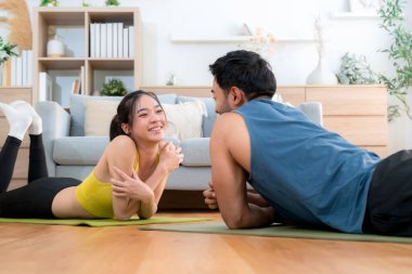 Genç Asyalı çift evdeki oturma odasında beşlik çakarken tahtayla antrenman yapıyor. Erkek ve kadın birlikte meydan okuma, motivasyon ve sağlık için kas gücü eğitimi alıyor..