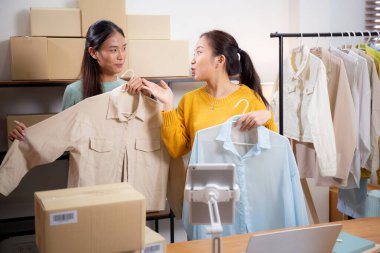 İki genç Asyalı kadın online giyim mağazasında yaşarken, evde sosyal tabletle giysi satışı yaparken, girişimci çevrimiçi kıyafet satışı ve sunumu için çevrimiçi satış yapıyor..