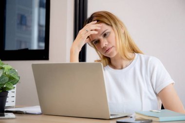 Mutsuz Kafkasyalı genç iş kadını masadaki dizüstü bilgisayarını kullanıyor. Ofiste stresli ve bitkin durumda. İş kadını hayal kırıklığına uğramış ve kaygılı bir şekilde dizüstü bilgisayarda çalışıyor..