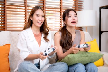 İki Asyalı kadın, evdeki rahat bir oturma odasında bilgisayar oyunu oynuyorlar. Eğlence, arkadaşlık ve neşeli bir yaşam tarzı. Asyalı arkadaşlar, eğlence ve oyun paylaşımının keyfini çıkarıyorlar..