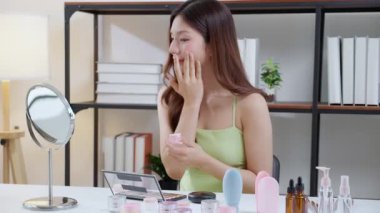 Güzel, genç Asyalı bir kadın evde aynaya bakarken kırışıklıklar için yüzüne krem sürüyor, güzel bir kadın yanağına losyon nemlendirici sürüyor, cilt bakımı ve güzellik, rahat bir şekilde kendine bakım yapıyor..