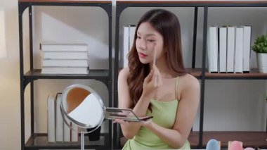 Yanağına bir ayna, güzellik ve kozmetik ile makyaj yapan mutlu, genç Asyalı bir kadın güzel, rahat bir yaşam tarzı, tatmin olmuş ve kozmetolojisi olan bir kadın..