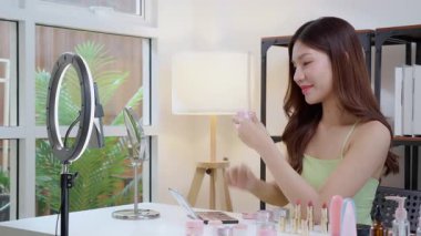 Sosyal medyada kozmetik ürünü sunan ve gözden geçiren Asyalı genç bir kadın, cilt kremi ürünlerini telefonla, canlı yayında ya da yayında inceleyen güzellik uzmanı, içerik yaratıcısı.