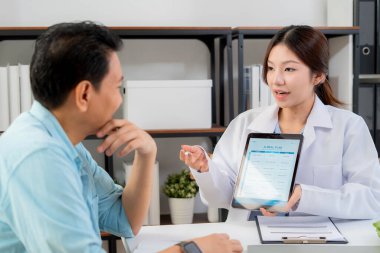 Asyalı beslenme uzmanı, AI ile kişiselleştirilmiş yemek planını sağlık hizmetleri danışmanlığı sırasında hastaya açıklamak için tablet kullanıyor, sağlıklı yaşam tarzı, kadın diyetçisi, tablette yapay zekayla beslenme planı gösteriyor..