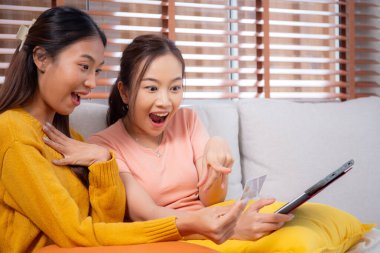 Kanepede oturan iki genç Asyalı kadın internet üzerinden tablet bilgisayar alışverişi yapıyor. İnternete kredi kartı satın alıyor, iş, alım ve ödeme, iş ve finans ile kadın ödemesi yapıyor..