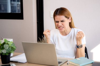 Mutsuz Kafkasyalı genç iş kadını masadaki dizüstü bilgisayarını kullanıyor. Ofiste stresli ve bitkin durumda. İş kadını hayal kırıklığına uğramış ve kaygılı bir şekilde dizüstü bilgisayarda çalışıyor..