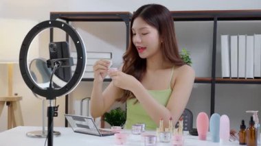 Sosyal medyada kozmetik ürünü sunan ve gözden geçiren Asyalı genç bir kadın, cilt kremi ürünlerini telefonla, canlı yayında ya da yayında inceleyen güzellik uzmanı, içerik yaratıcısı.