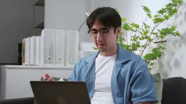 Merkez ofiste uzaktan kumandalı beyaz bir adam, video görüşmesi sırasında dizüstü bilgisayar kullanıyor, dijital göçebe, oturma odasında küçük iş planlama için erkek video çağrısı, çevrimiçi işbirliği.