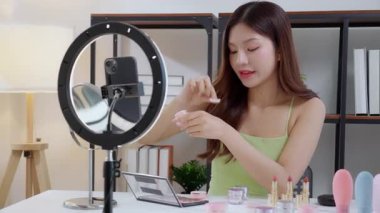 Sosyal medyada kozmetik ürünü sunan ve gözden geçiren Asyalı genç bir kadın, cilt kremi ürünlerini telefonla, canlı yayında ya da yayında inceleyen güzellik uzmanı, içerik yaratıcısı.