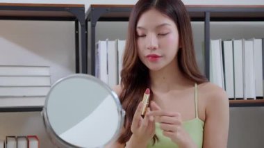 Genç Asyalı kadın evde aynaya ruj sürüyor, güzellik ve makyaj rutini kişisel bakım, kozmetik ve rahatlama, dudaklı ağız, güzellik, ayna, yaşam tarzı ve makyaj.