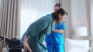 Tekerlekli sandalyeden kanepeye taşınırken hareket kabiliyeti kısıtlı olan bakıcı, evdeki oturma odasında tekerlekli sandalyeden kanepeye taşınan hastaya yardım eden hemşire, rehabilitasyon ve yardım..