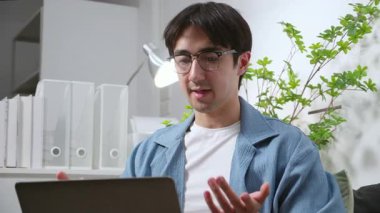 Merkez ofiste uzaktan kumandalı beyaz bir adam, video görüşmesi sırasında dizüstü bilgisayar kullanıyor, dijital göçebe, oturma odasında küçük iş planlama için erkek video çağrısı, çevrimiçi işbirliği.